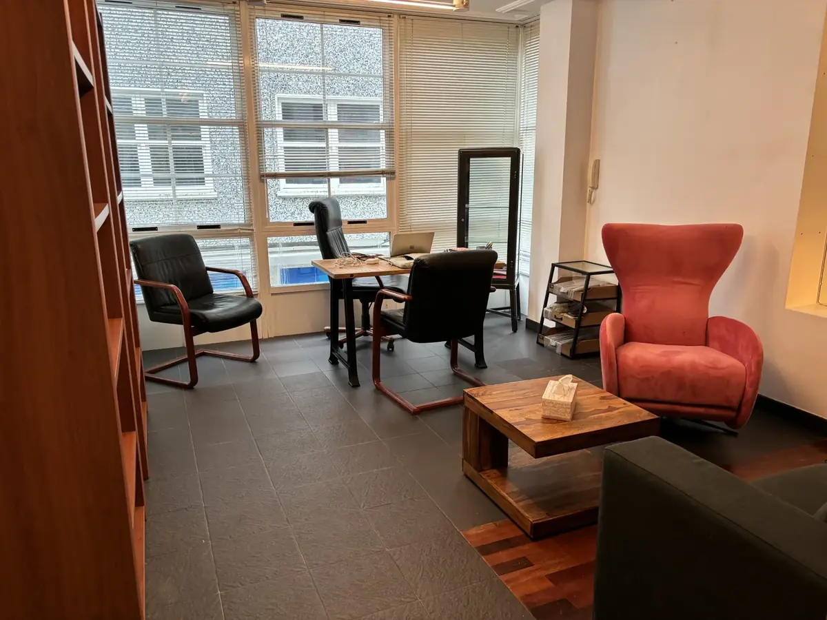 Vista general de la consulta con ventanales, mesa de trabajo, sillones de piel y butaca rosa
